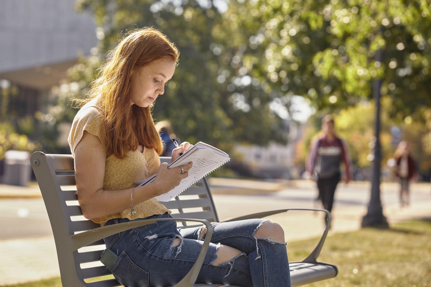 A <a href='http://safety.5g-taiou-wifi.net'>博彩网址大全</a> student reads on a bench along Campus Drive.